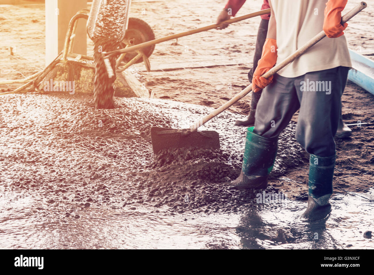 man workers spreading freshly poured concrete mix on building with vintage tone. Stock Photo