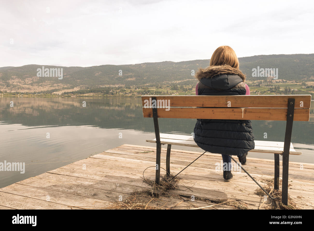 Beautiful girl on a bench looking at the lake Stock Photo