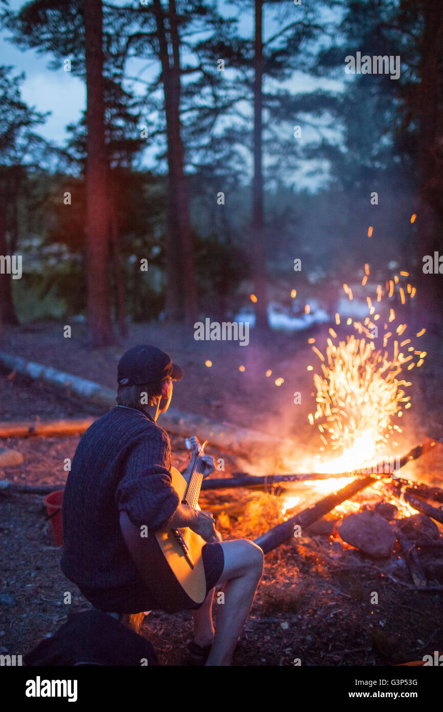 Sweden, Medelpad, Man playing guitar by campfire Stock Photo