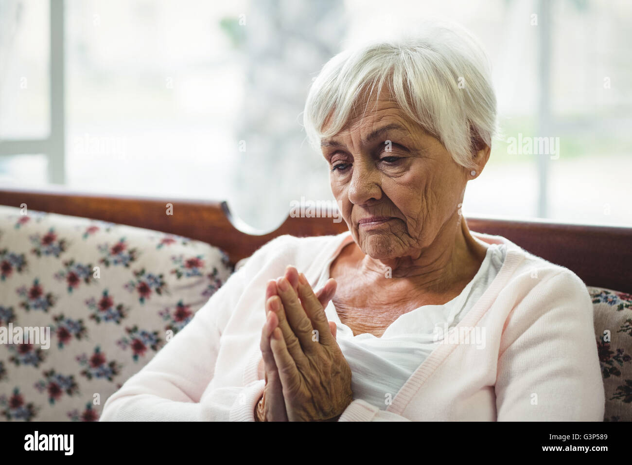 Senior woman praying in living room Stock Photo