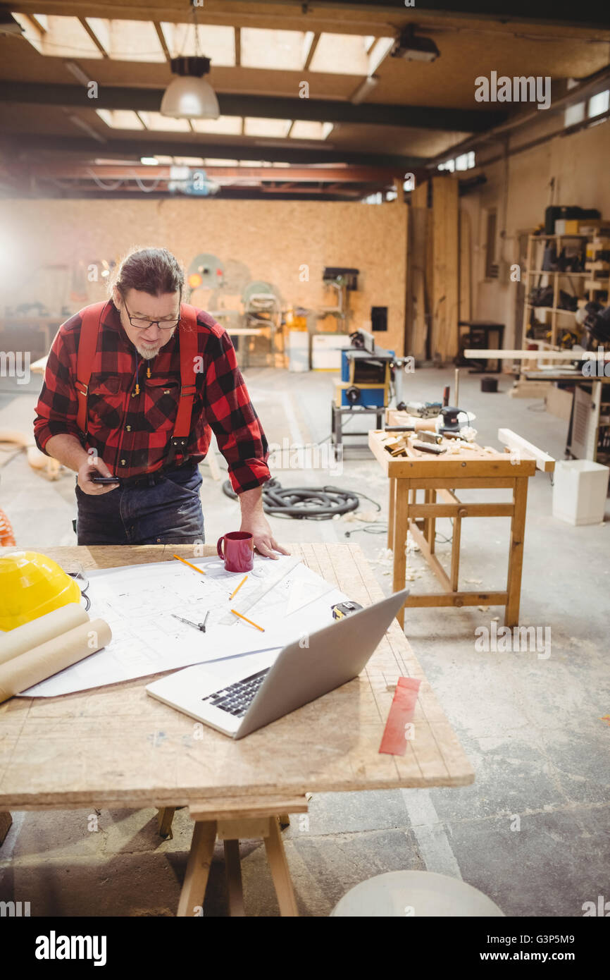 Carpenter using his smartphone while reading plans Stock Photo