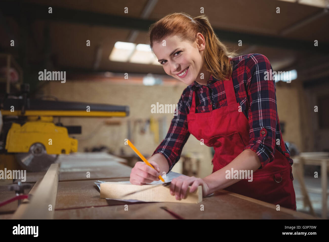 Female carpenter marking on wooden plank with pencil in workshop Stock Photo