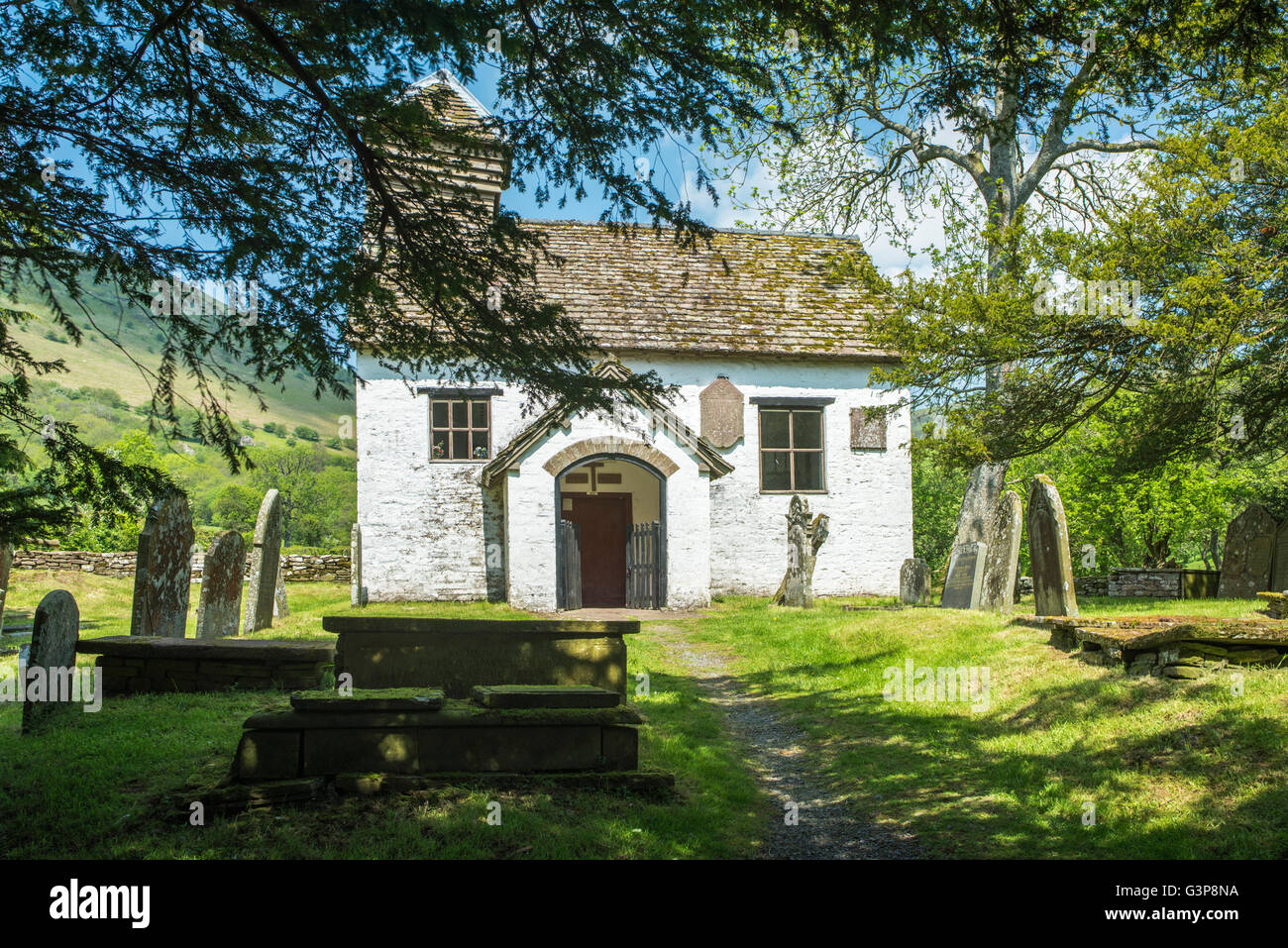 Small whitewashed church / chapel with graveyard in a valley. Stock Photo