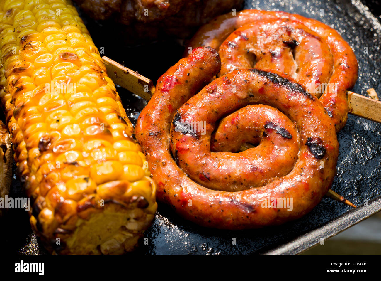 Circular coiled sausages on a barbeque. Spiral of sausage with a wooden skewer. Corn on the cob or maize on a barbecue. Stock Photo