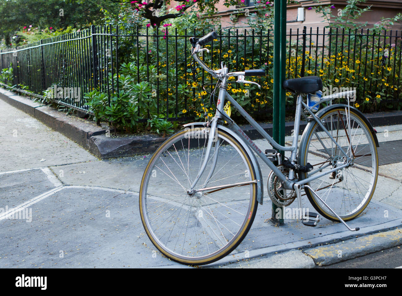 Bicycle leaning on a sign post with the coffee cup left over from commute in an urban neighborhood sidewalks and gardens Stock Photo