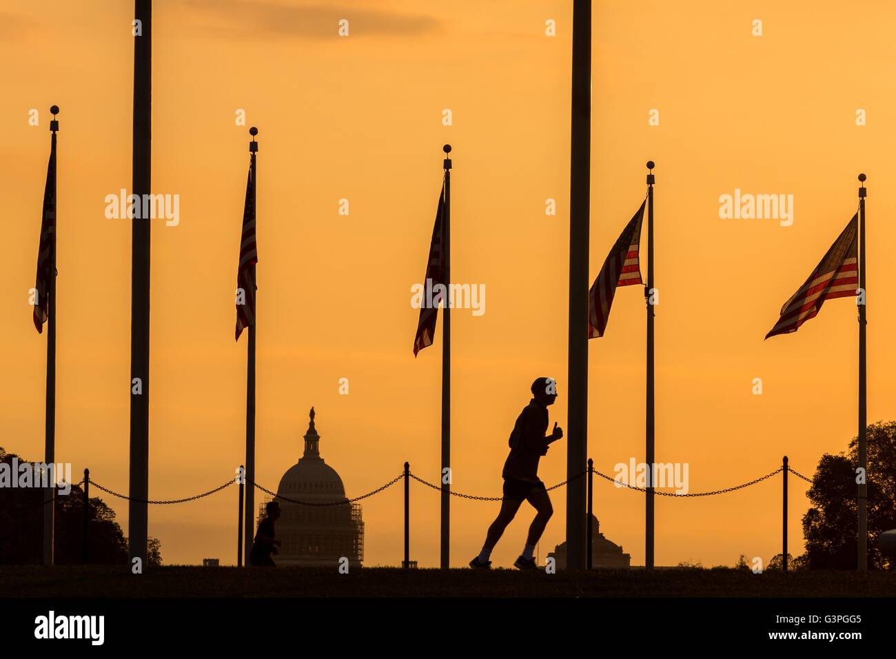 A runner passes flags around the Washington Monument silhouetted by sunset in Washington, DC. Stock Photo