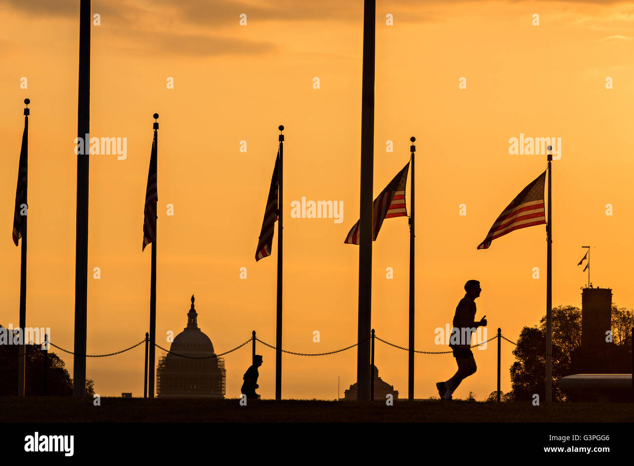 A runner passes flags around the Washington Monument silhouetted by sunset in Washington, DC. Stock Photo