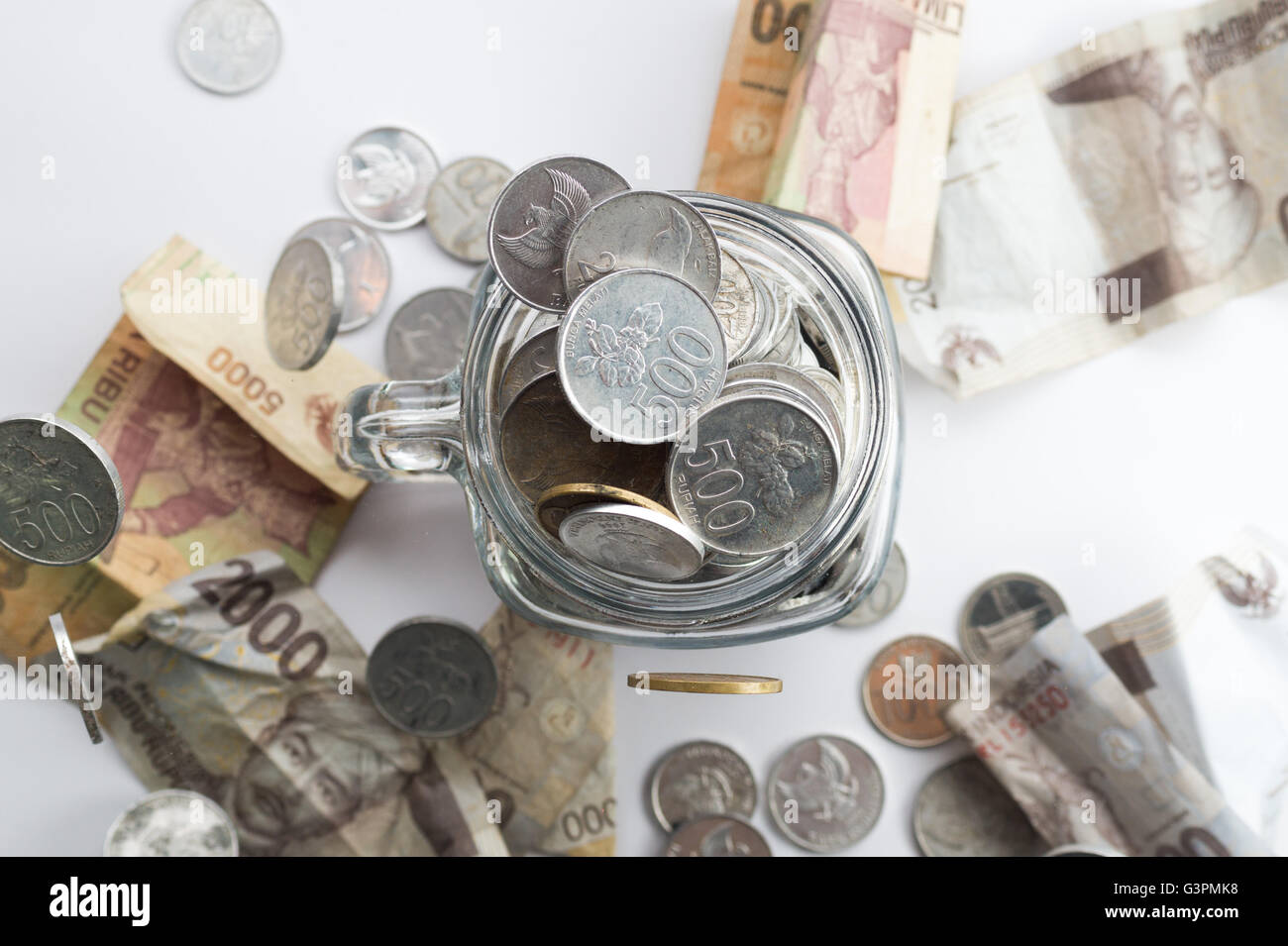 Rupiah Coin inside of Jar with money scatter around the jar Stock Photo