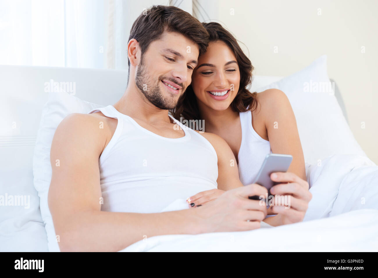 Young sweet couple in bed looking at a mobile phone at home Stock Photo ...