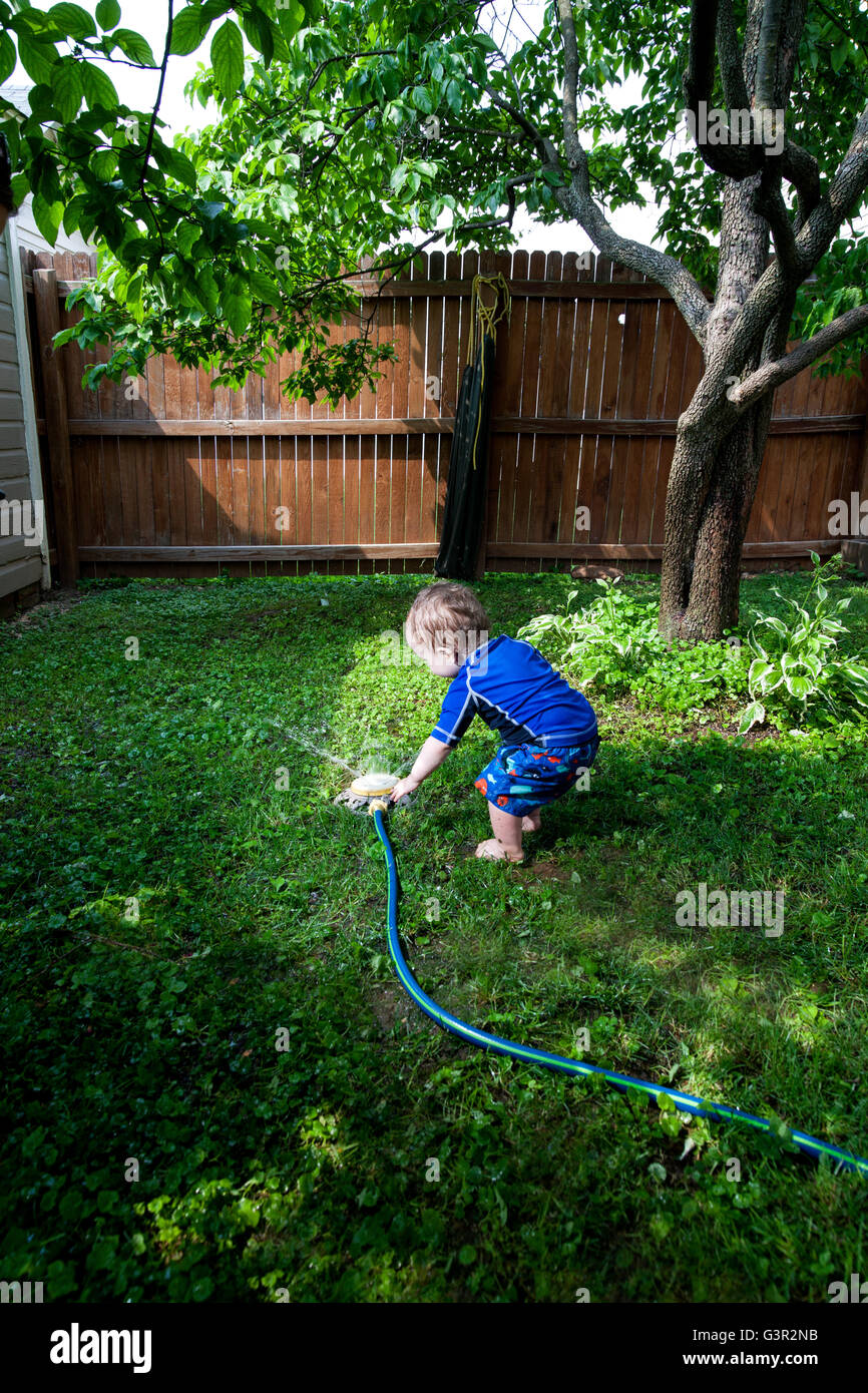 Baby Caucasian Boy and Mother playing in his backyard with a garden sprinkler Stock Photo