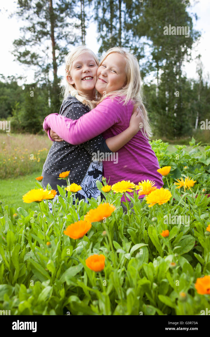 Sweden, Medelpad, Two girls (10-11, 12-13) standing in yellow flowers and hugging Stock Photo