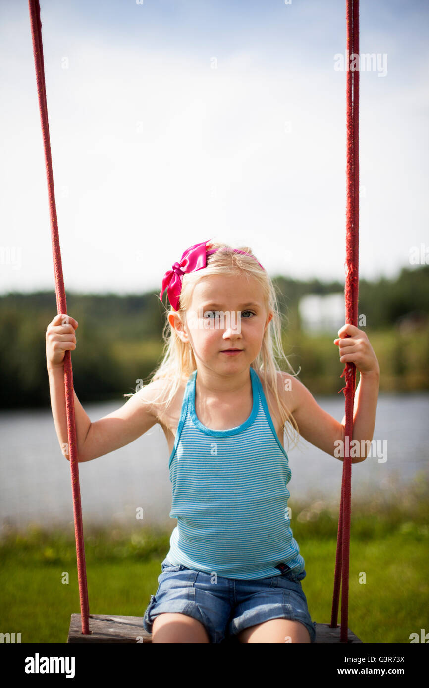 Sweden, Medelpad, Girl (6-7) sitting on rope swing Stock Photo