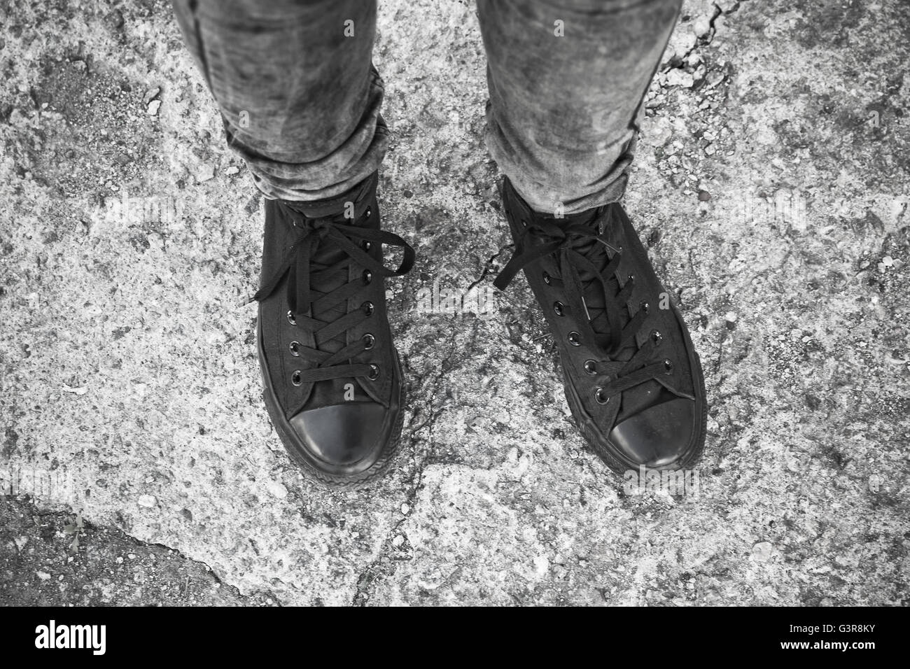Teenager fashion theme, feet in black gumshoes and gray jeans standing on rough concrete floor Stock Photo