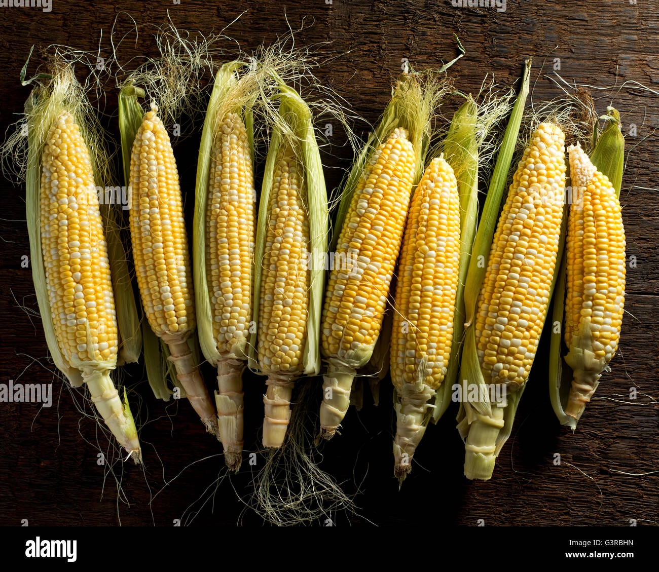 Fresh local organic corn on the cob against a rustic harvest table background. Stock Photo