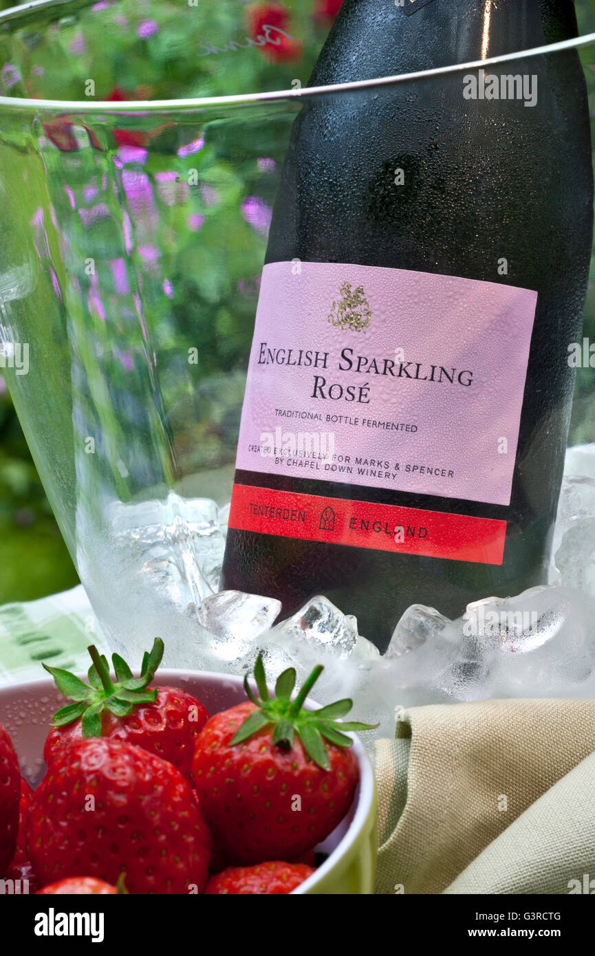 English Sparkling Rosé wine bottle in iced wine chiller with bowl of fresh strawberries on alfresco garden picnic table Stock Photo