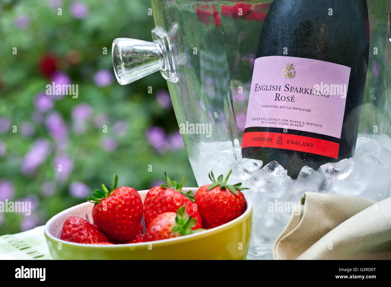 English Sparkling Rosé wine bottle in iced wine chiller with bowl of fresh strawberries on summer staycation alfresco floral table Stock Photo