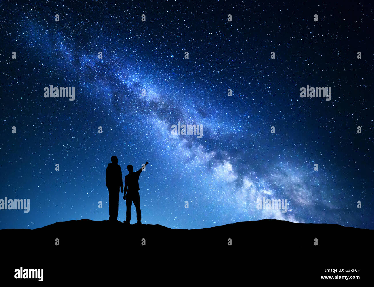 Milky Way with silhouette of a family. Father and a son who pointing finger in night starry sky on the mountain. Night landscape Stock Photo