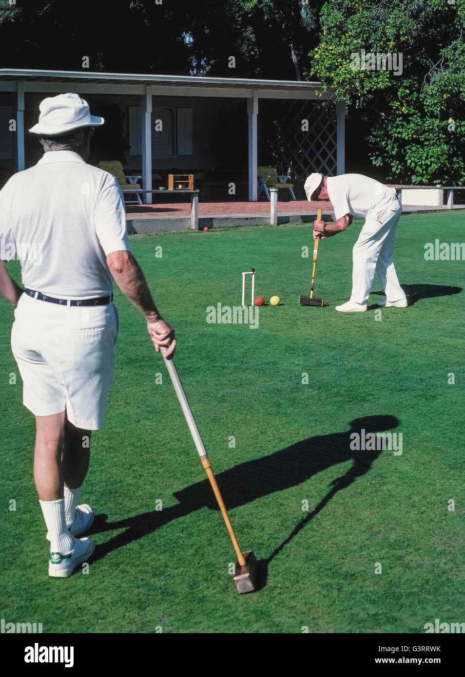 The traditional game of croquet is a popular activity for members of the the local croquet club who dress in all white apparel, as well as for guests at The Inn at Rancho Santa Fe, both of whom play on the sprawling front lawn of that luxury hotel in San Diego County, California, USA. Club members follow the official rules of the U.S. Croquet Association for Six-Wicket American Croquet that specify the equipment to be used, including the mallets, balls, wickets and stake. Here a male club player strikes his yellow ball with a square wooden mallet into an opponent's red ball. Stock Photo