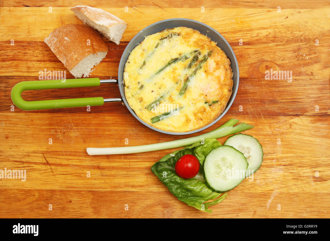 An individual Frittata in a pan with bread and salad on a wooden chopping board Stock Photo
