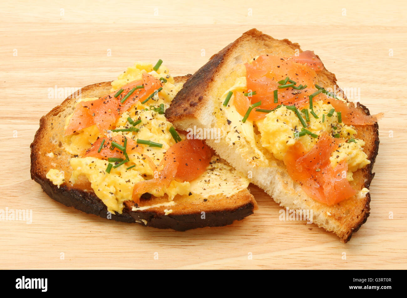 Scrambled egg with smoked salmon and chives on toasted crusty bread on a wooden board Stock Photo