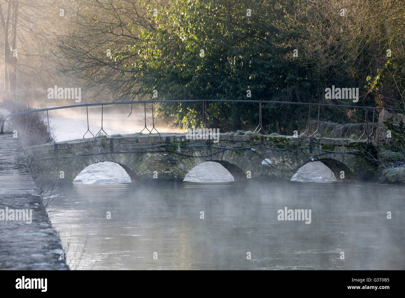 Arched footbridge over River Coln in mist, Bibury, Cotswolds, Gloucestershire, England, United Kingdom, Europe Stock Photo