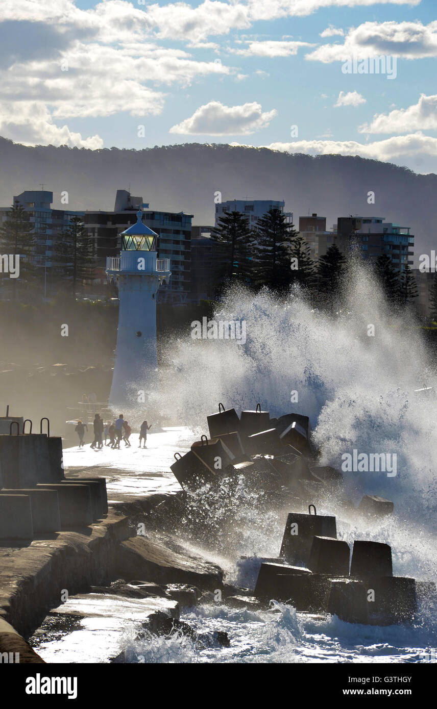 People splashed by big waves caused by storm surge breaking over Wollongong harbor breakwall near the lighthouse, NSW, Australia Stock Photo