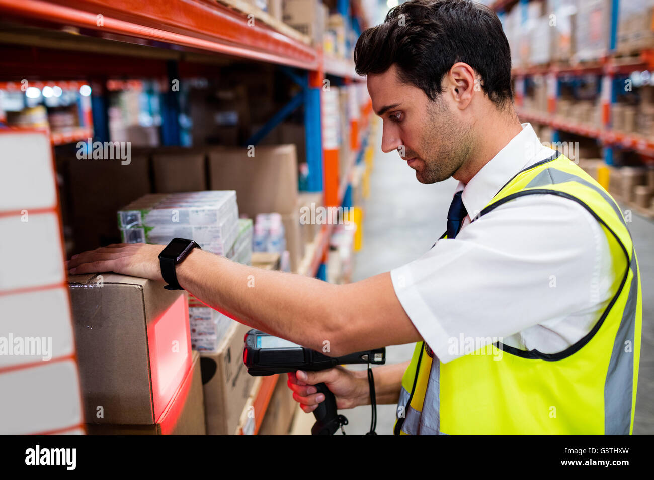 Warehouse manager with yellow coat scanning barcode on box Stock Photo