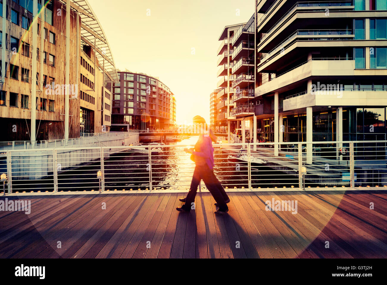 Norway, Oslo, Aker Brygge, Pedestrians on city bridge silhouetted against setting sun Stock Photo