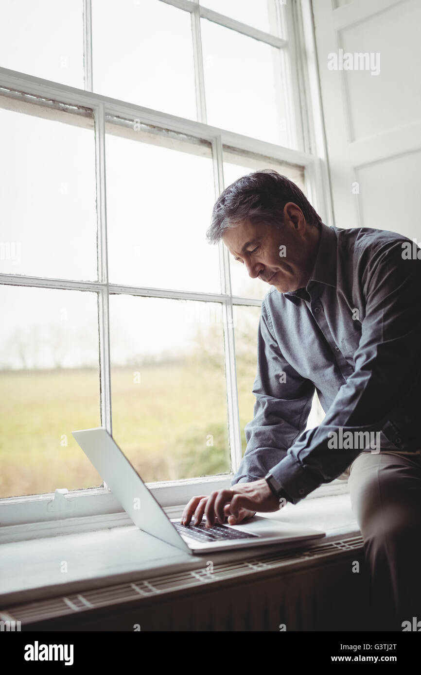 Mature man using laptop at window Stock Photo