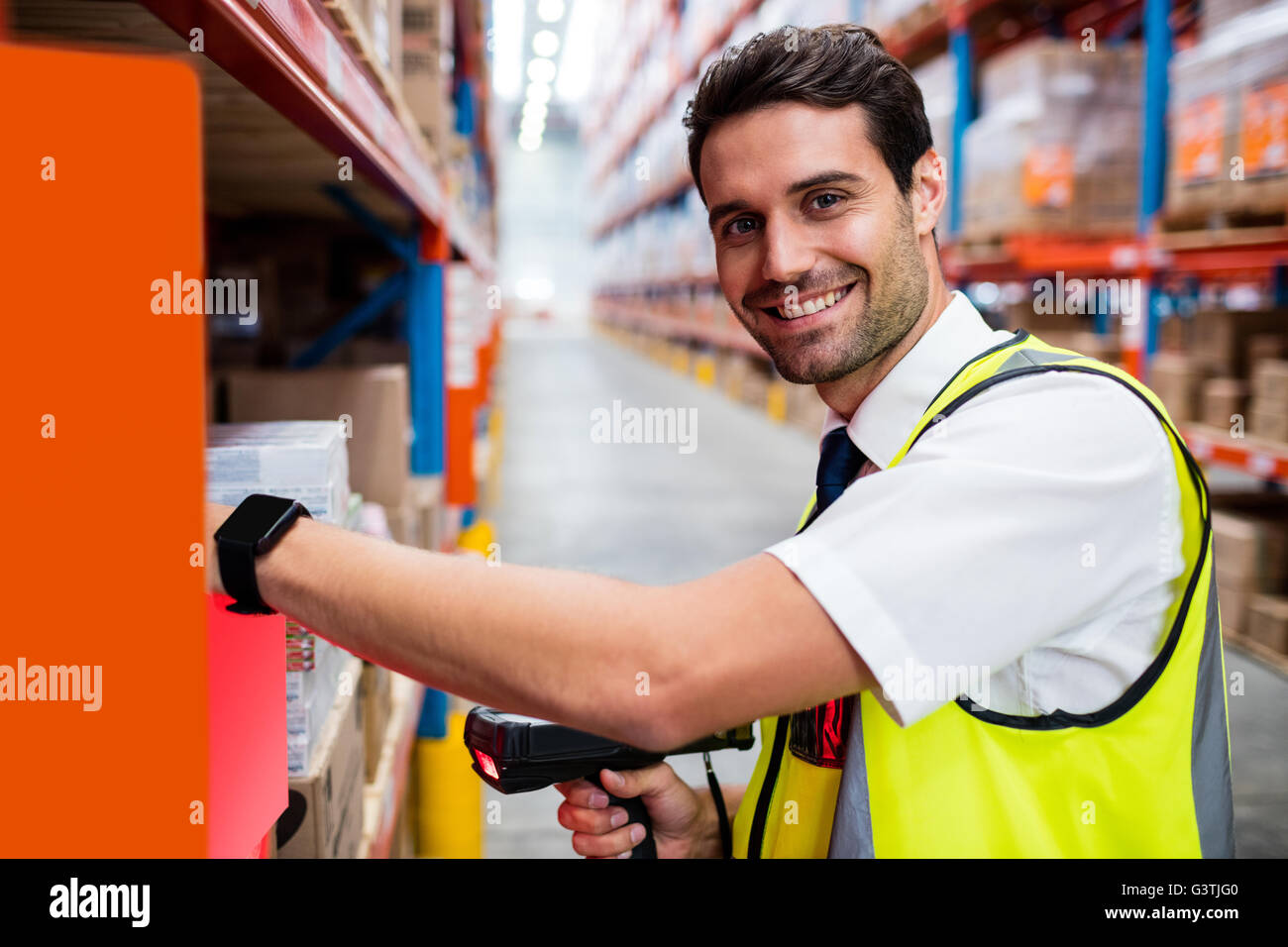 Smiling warehouse manager with yellow coat scanning barcode on box Stock Photo