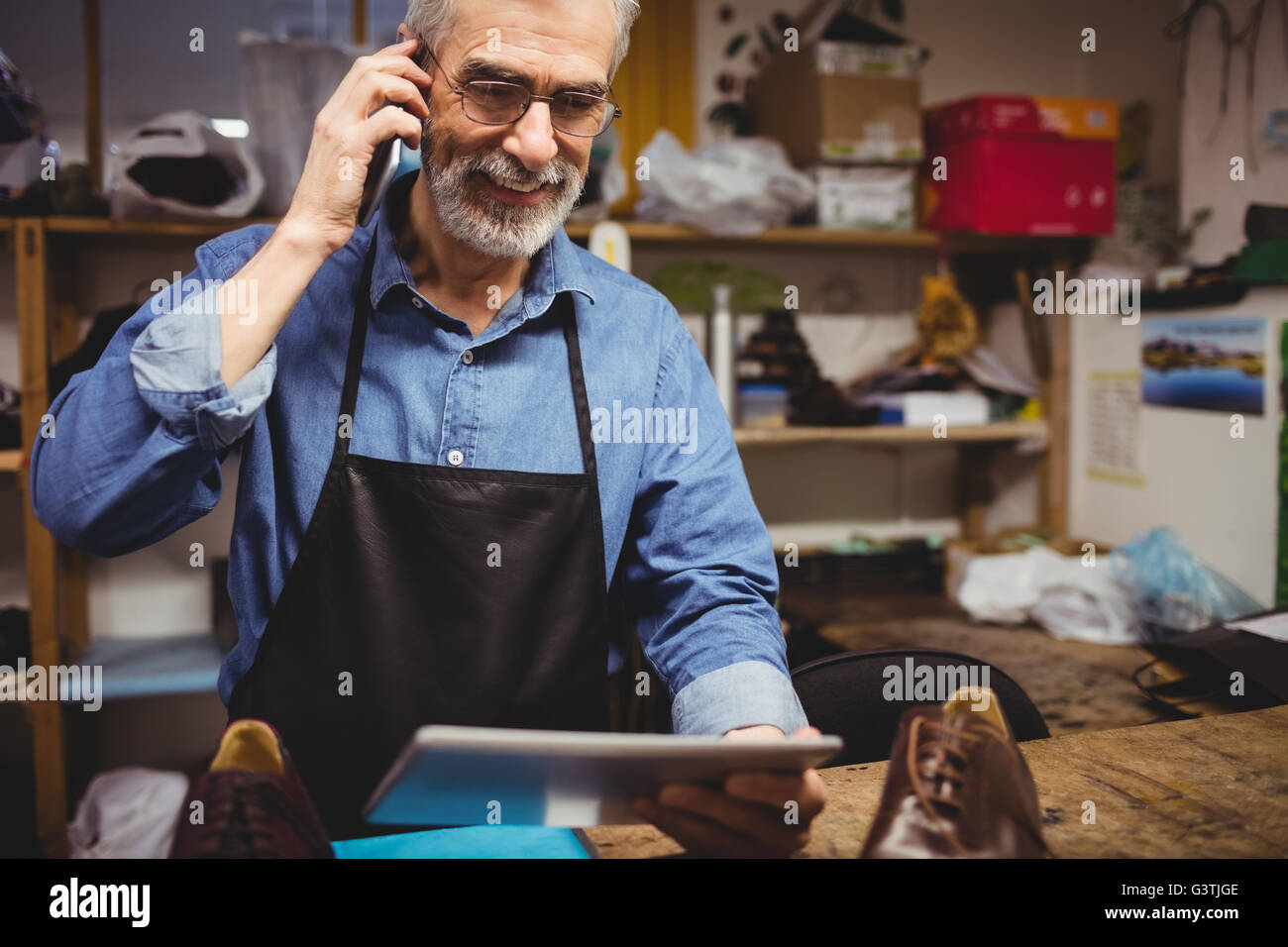 Cobbler calling with his mobile phone and holding a tablet computer Stock Photo