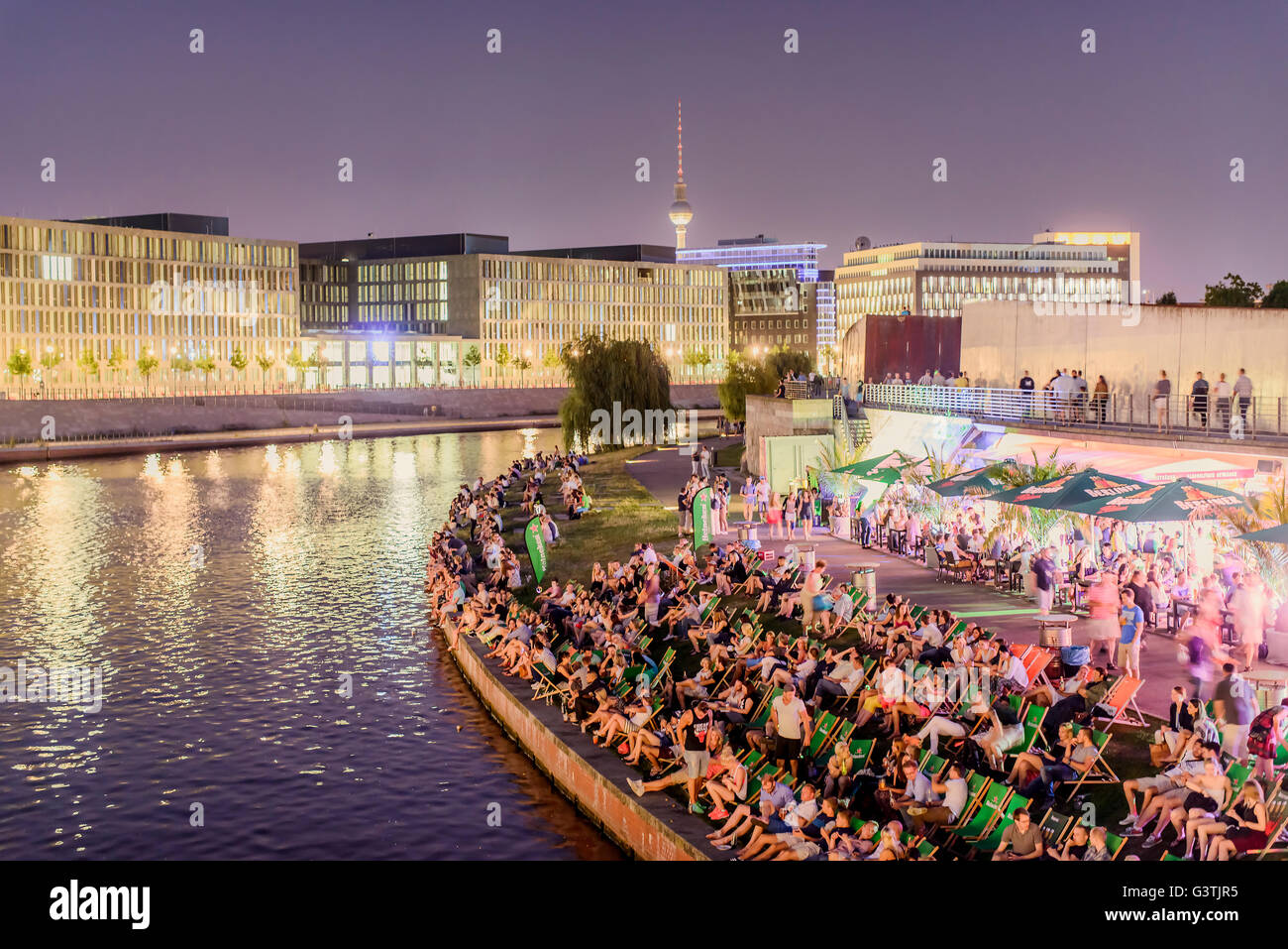 Germany, Berlin, Spree River, Crowd sitting in folding chairs on riverbank at night Stock Photo