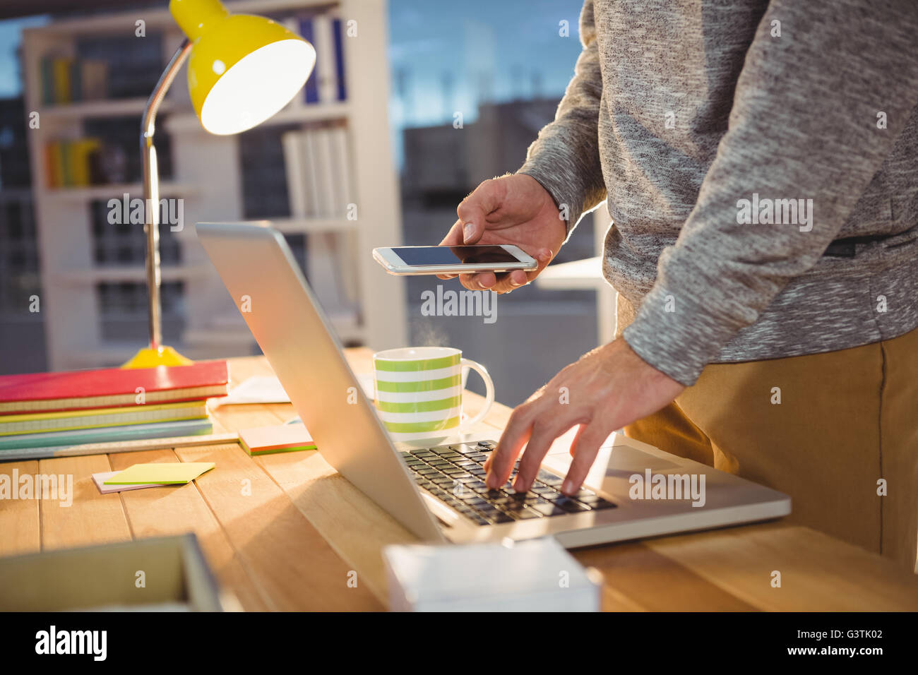 Man holding a phone and typing on the computer Stock Photo