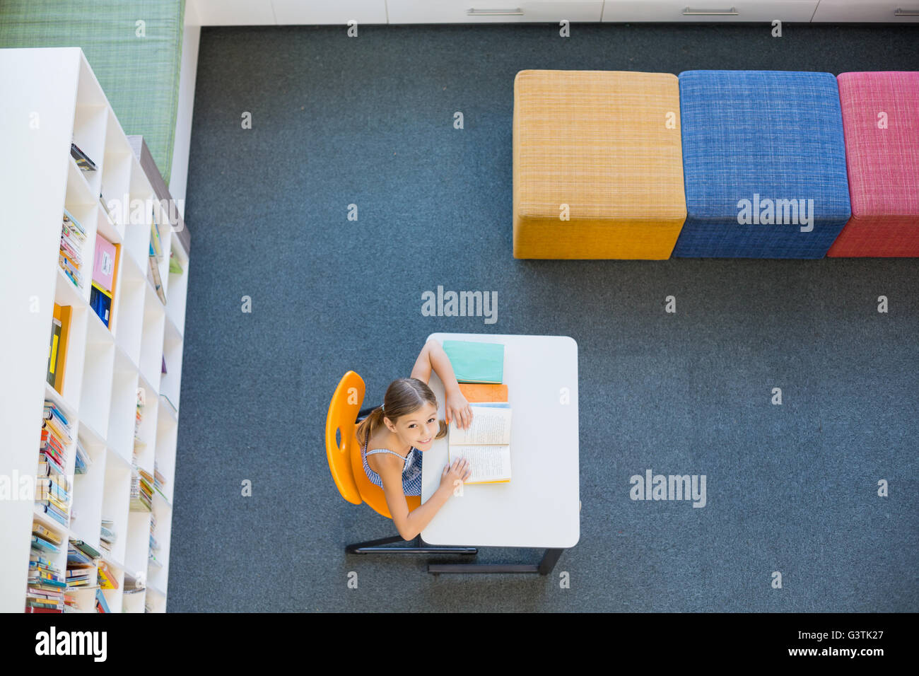 Smiling school girl reading a book in library Stock Photo - Alamy