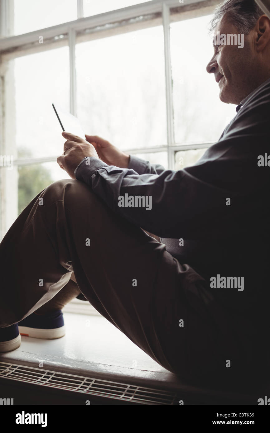 Profile view of mature man sitting at window and using tablet computer Stock Photo
