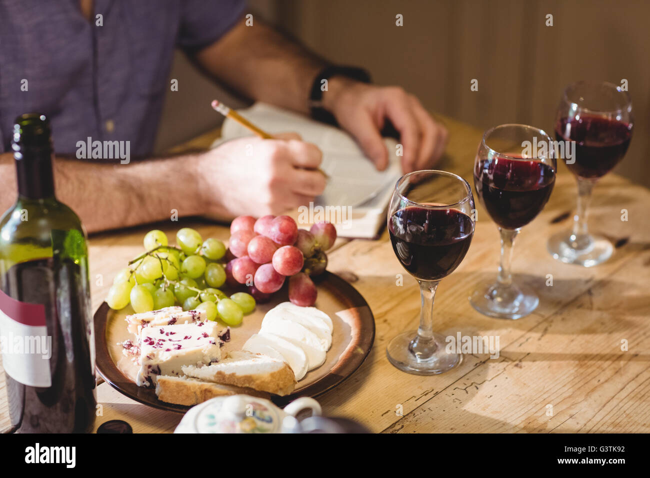 Cropped image of mature man writing in a book while tasting red wine and eating cheese Stock Photo