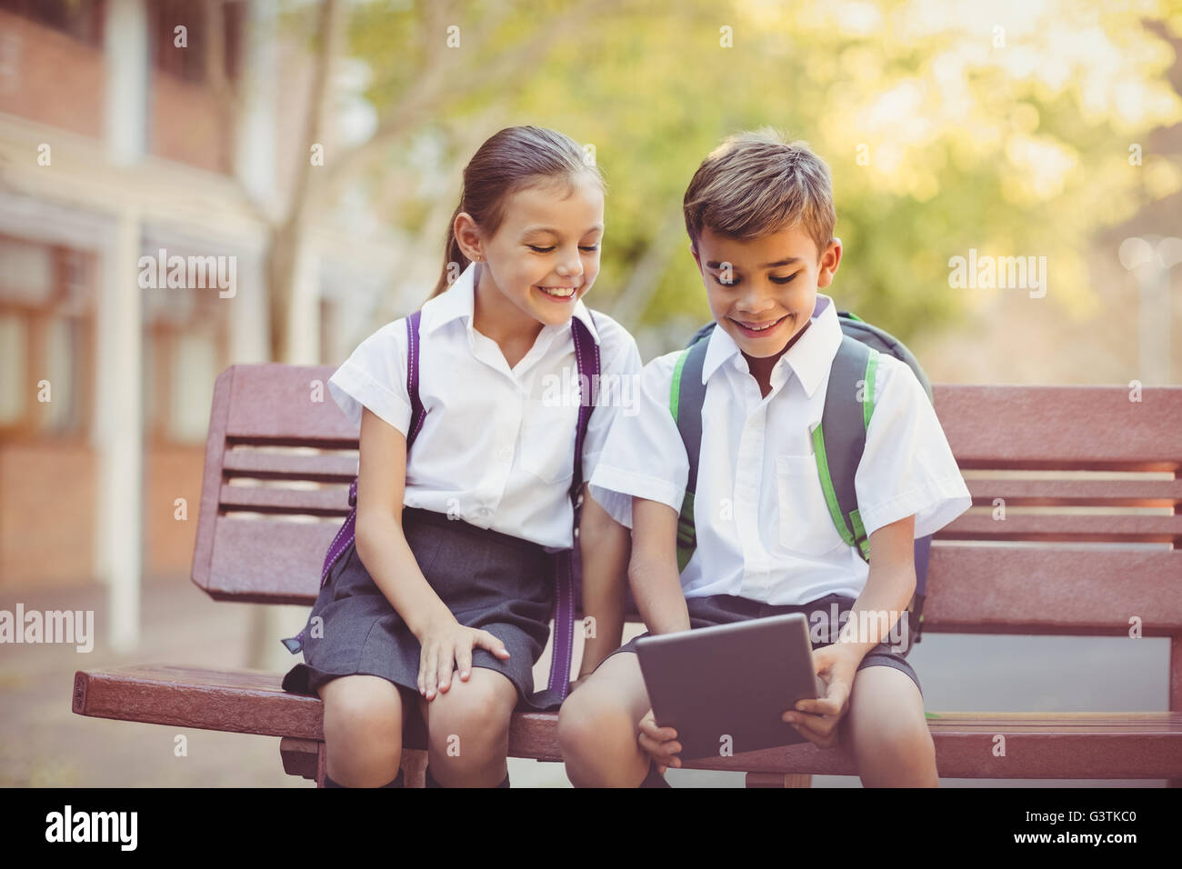 Happy school kids sitting on bench and using digital tablet Stock Photo