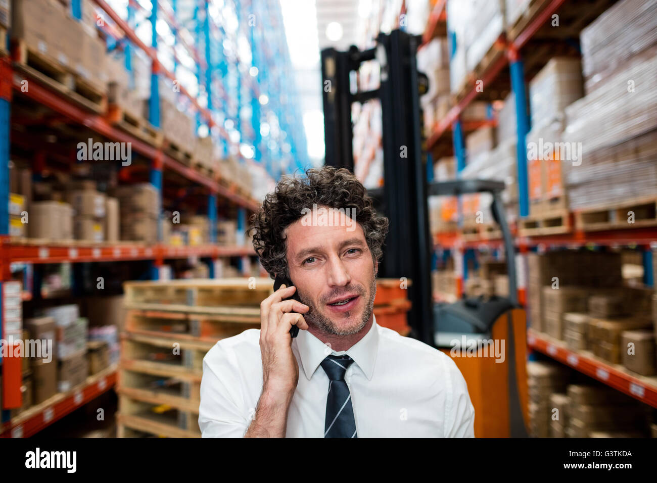 Warehouse manager giving phone call next to a forklift Stock Photo