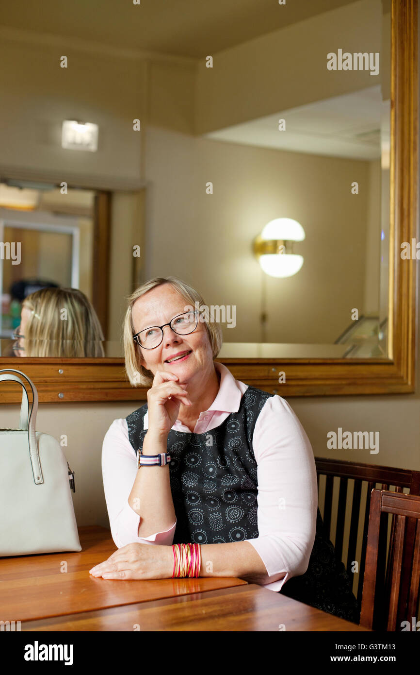 Finland, Smiling senior woman sitting at table Stock Photo