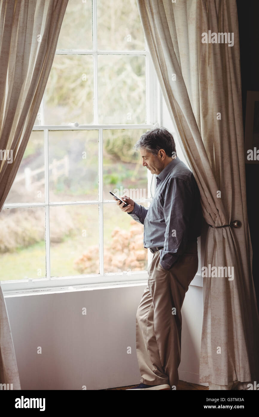 Mature man using mobile phone at window Stock Photo