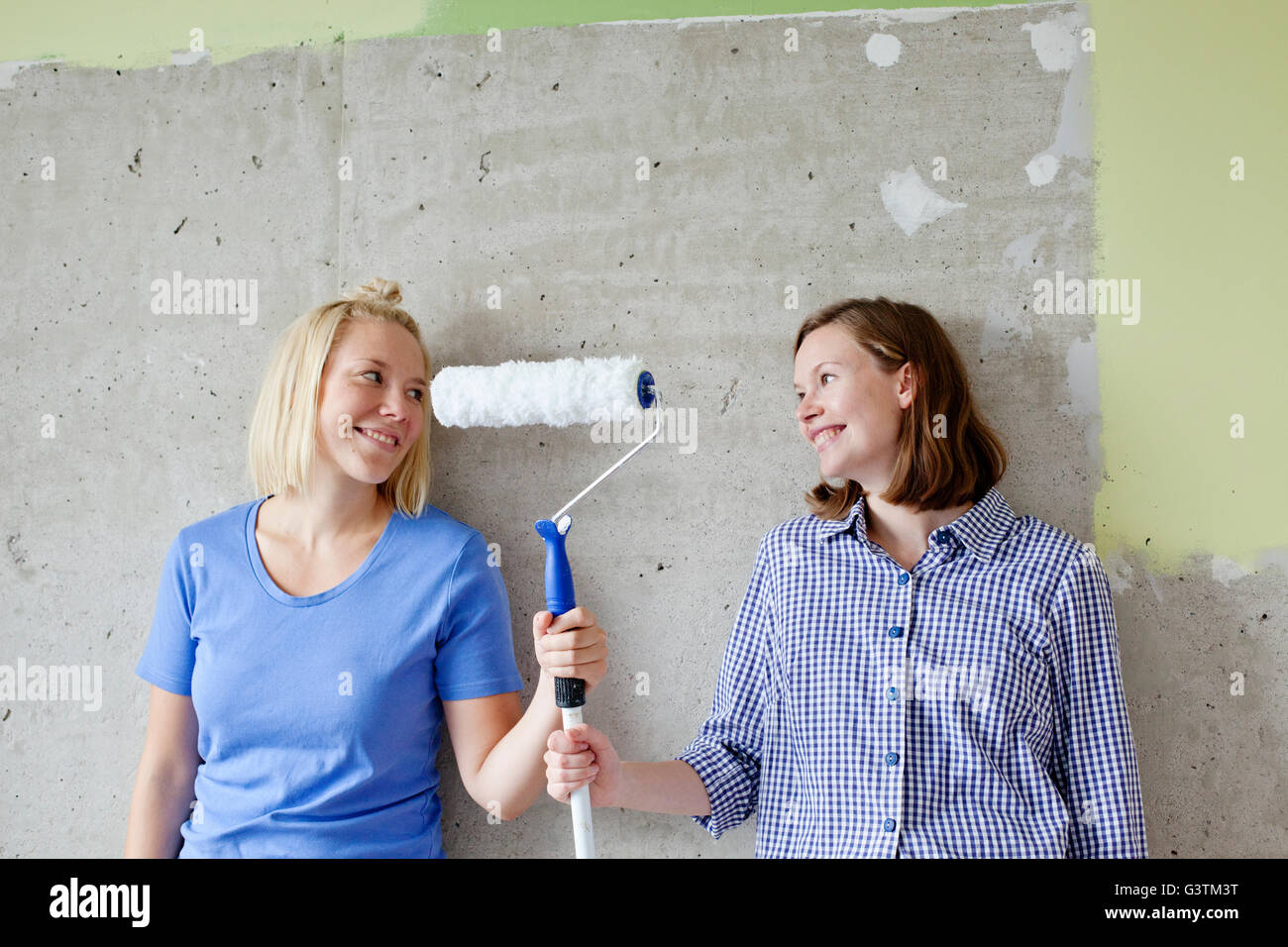 Finland, Young women standing by wall and holding paint roller Stock Photo