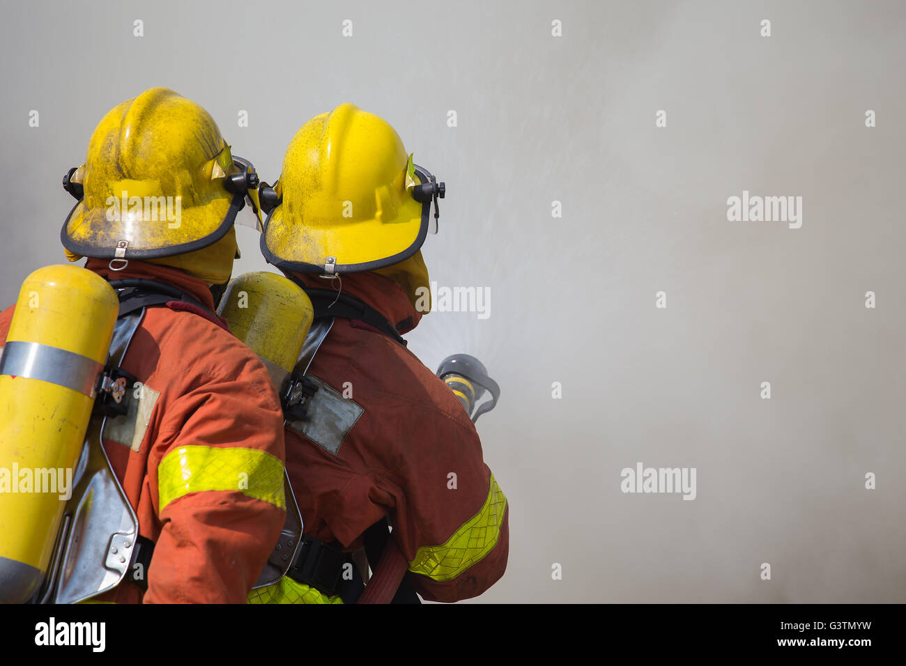 2 firemen spraying water in fire fighting with fire and dark smoke