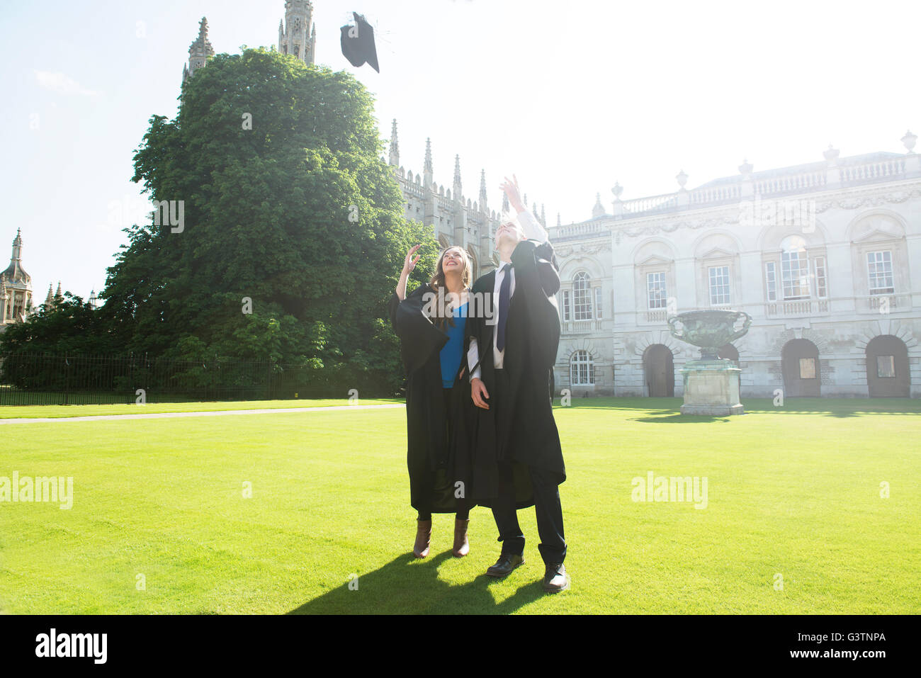 Two young students in graduation gowns throwing mortar boards into the air in celebration in the grounds of Cambridge University Stock Photo