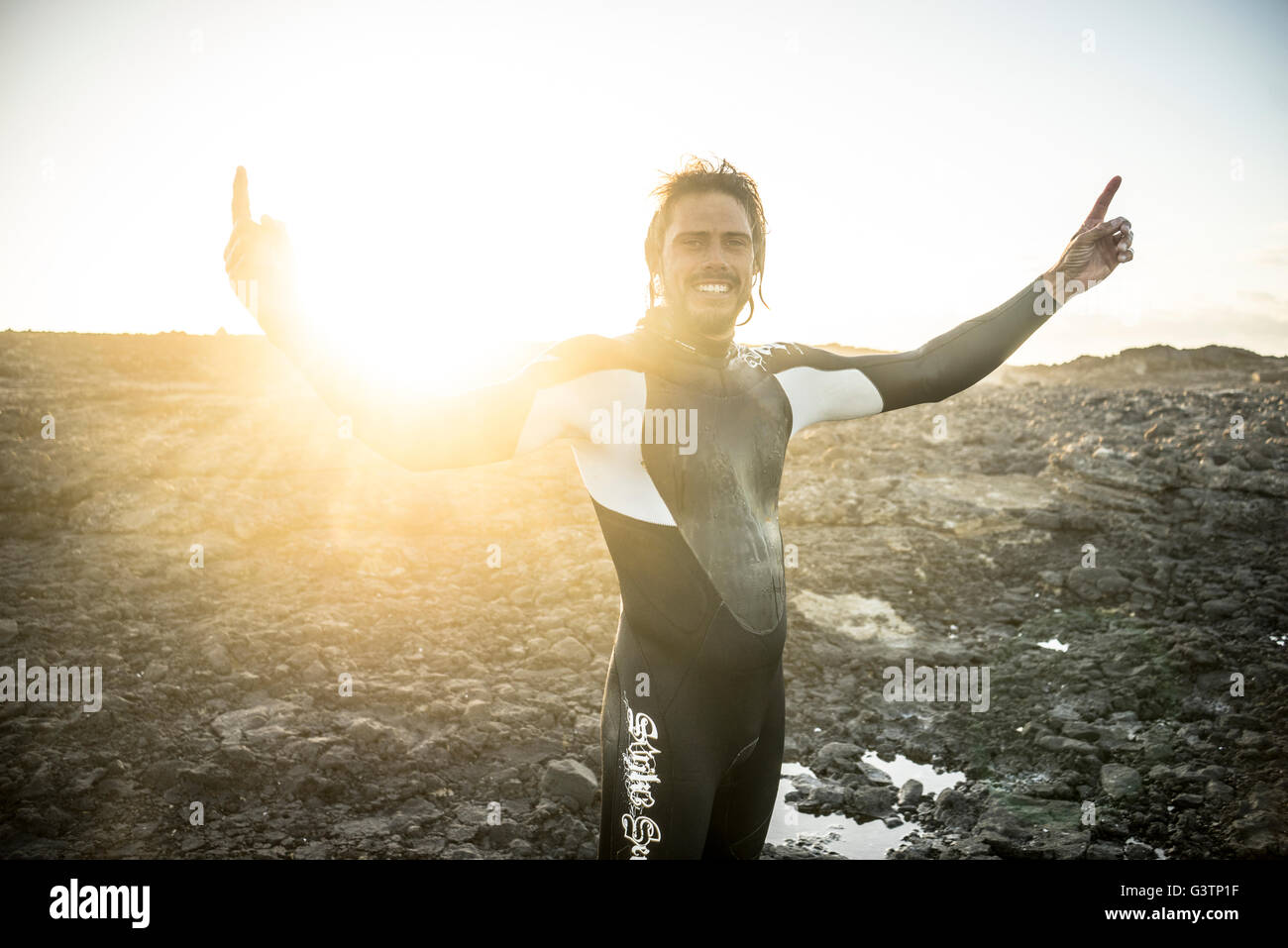 A surfer in a wetsuit raises his arms at Corralejo in Fuerteventura. Stock Photo