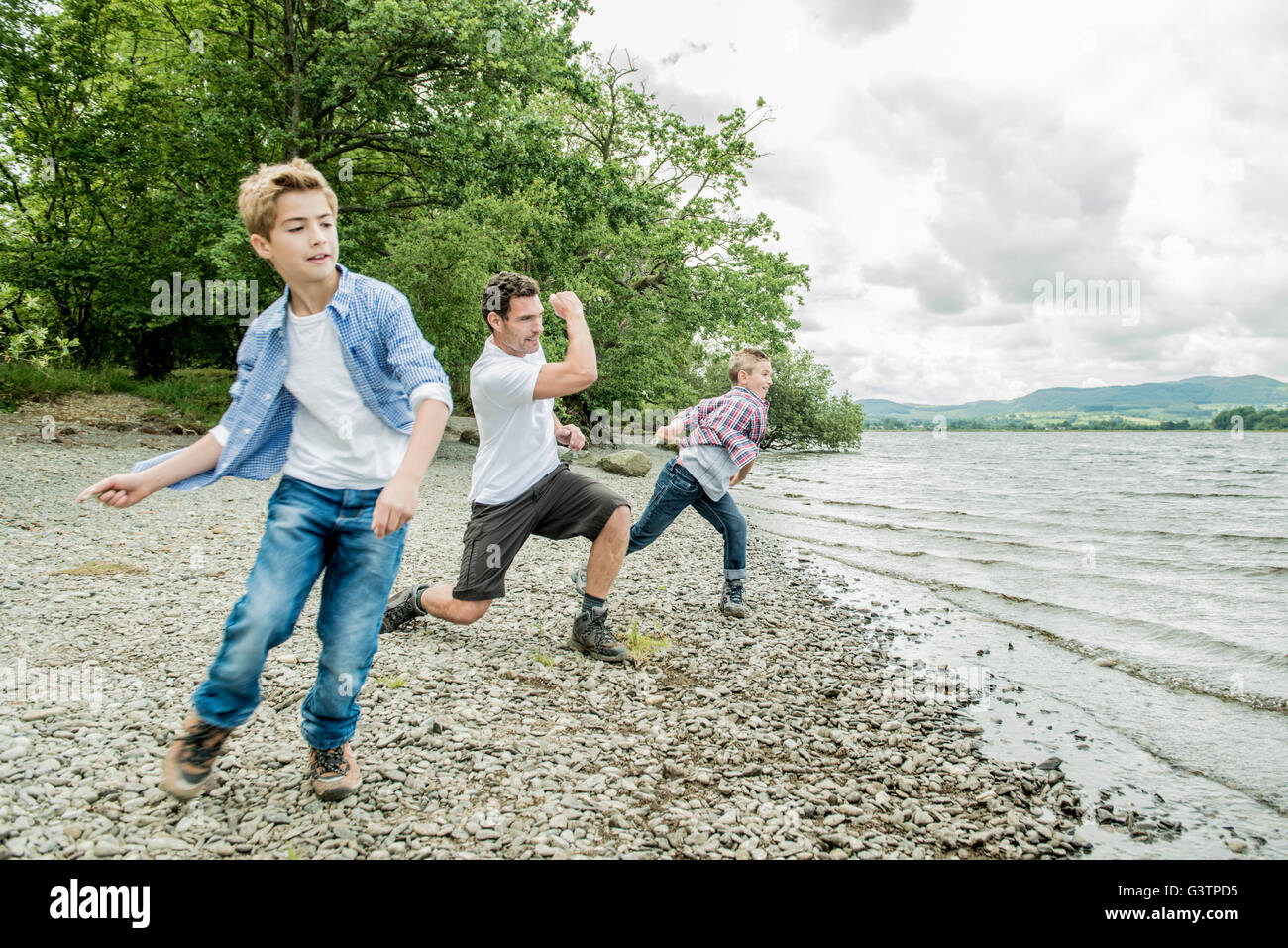A man and two boys skimming stones on the shore beside Bala Lake in