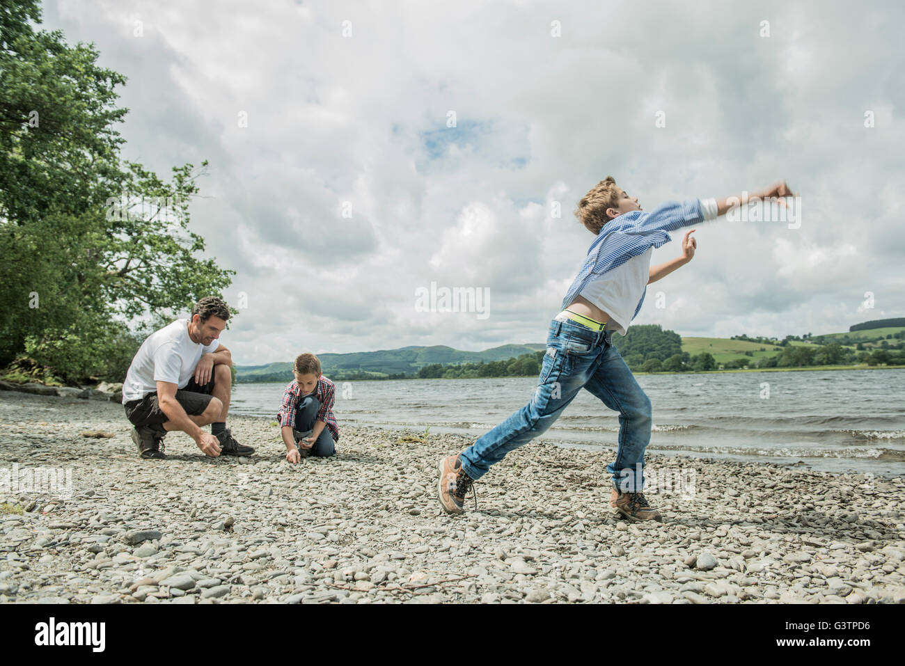 A man and two boys skimming stones on the shore beside Bala Lake in Wales. Stock Photo