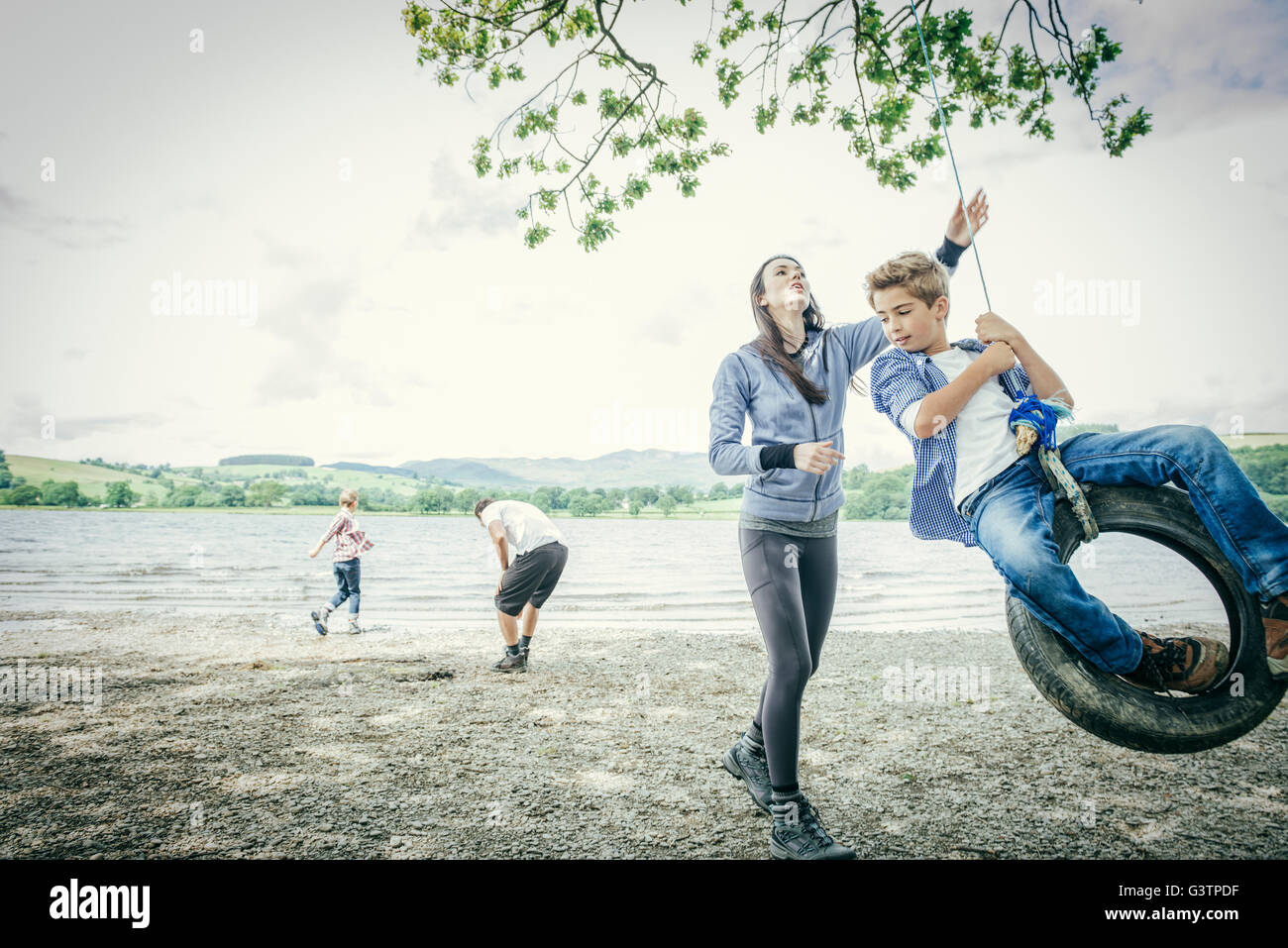 A family of four playing on a tyre hanging from a tree on the shore beside Bala Lake in Wales. Stock Photo