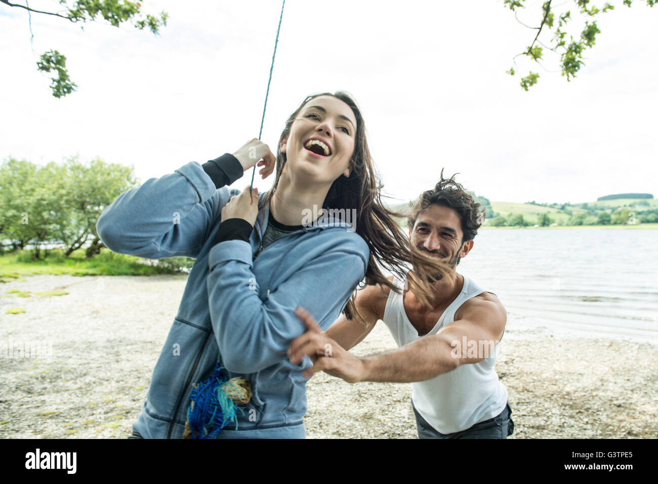 A man and a woman playing on a tyre hanging from a tree on the shore beside Bala Lake in Wales. Stock Photo