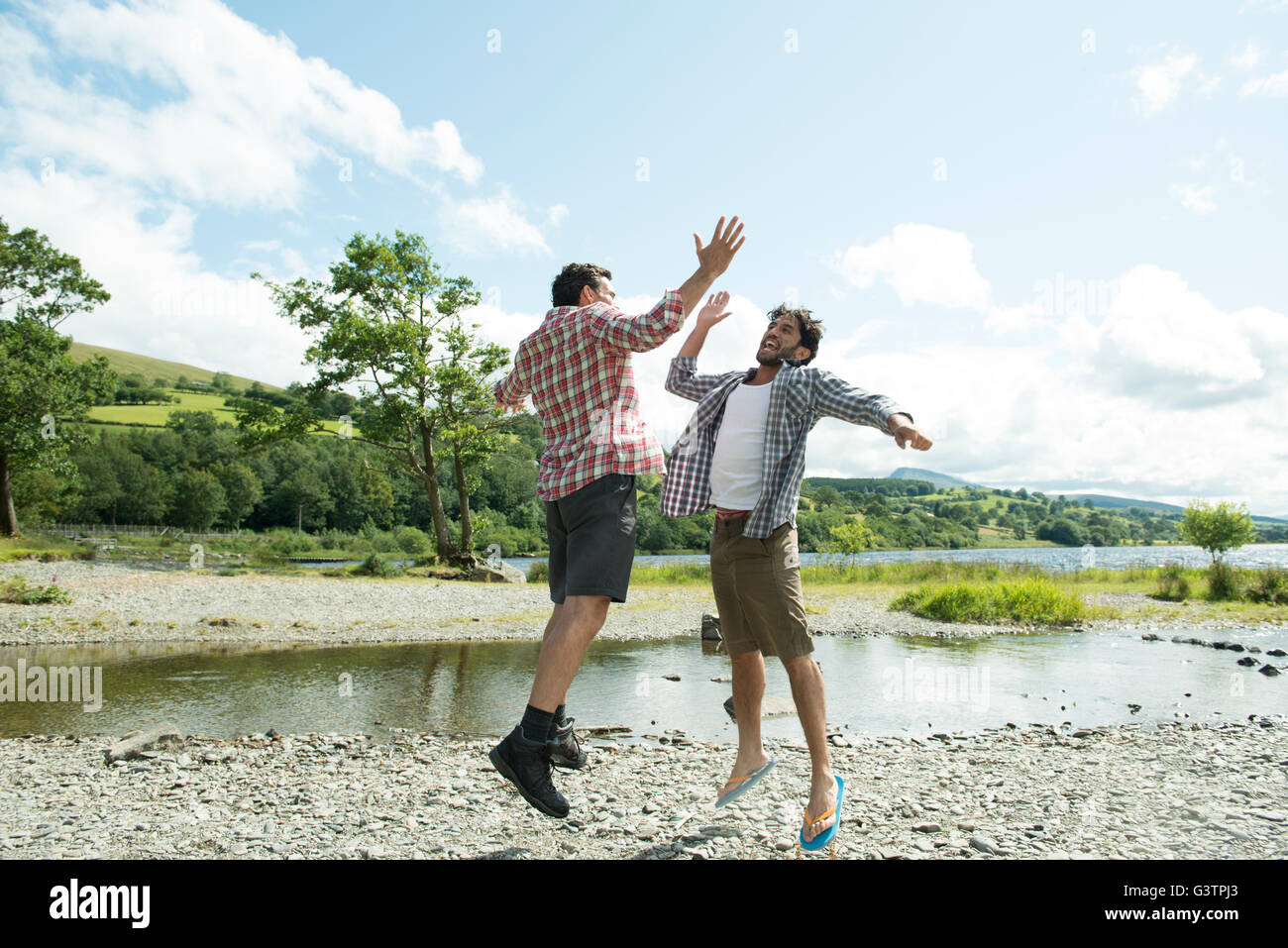 Two men leaping to high five near Bala Lake in Wales. Stock Photo