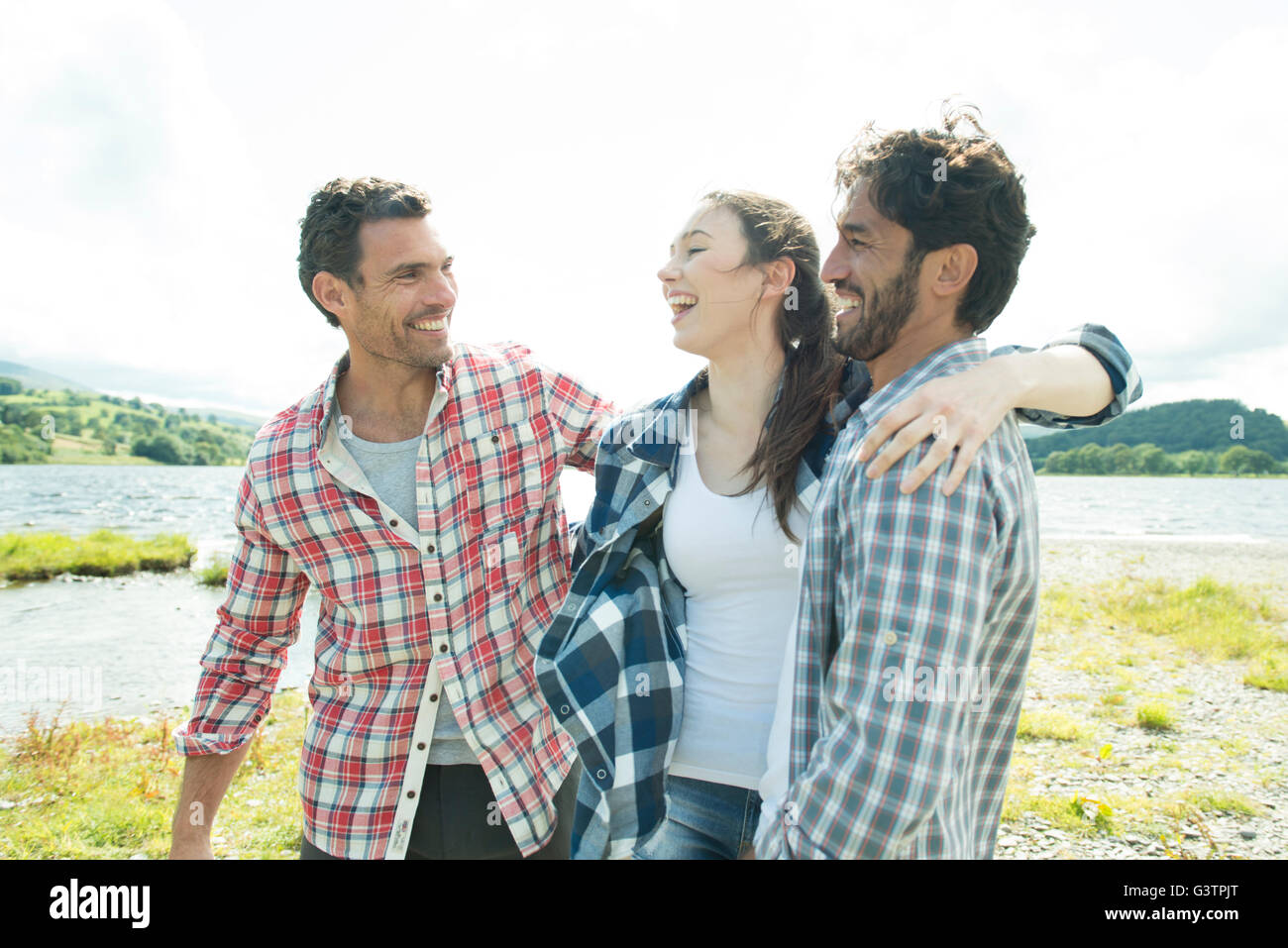 Three friends standing smiling on the shore of Bala Lake in Wales. Stock Photo